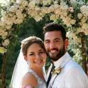 Una coppia di sposi felici sotto un arco fiorito.